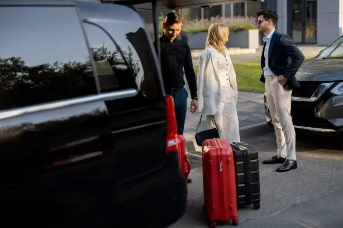 Chauffeur assisting clients with luggage near a luxury vehicle for Aurora limo service outside a modern building
