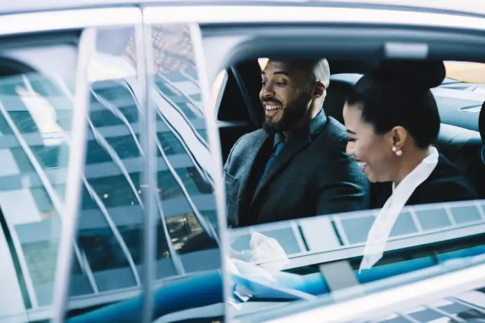 Two professionally dressed people smiling in the back seat of a luxury car, representing Belleville Limo Service.