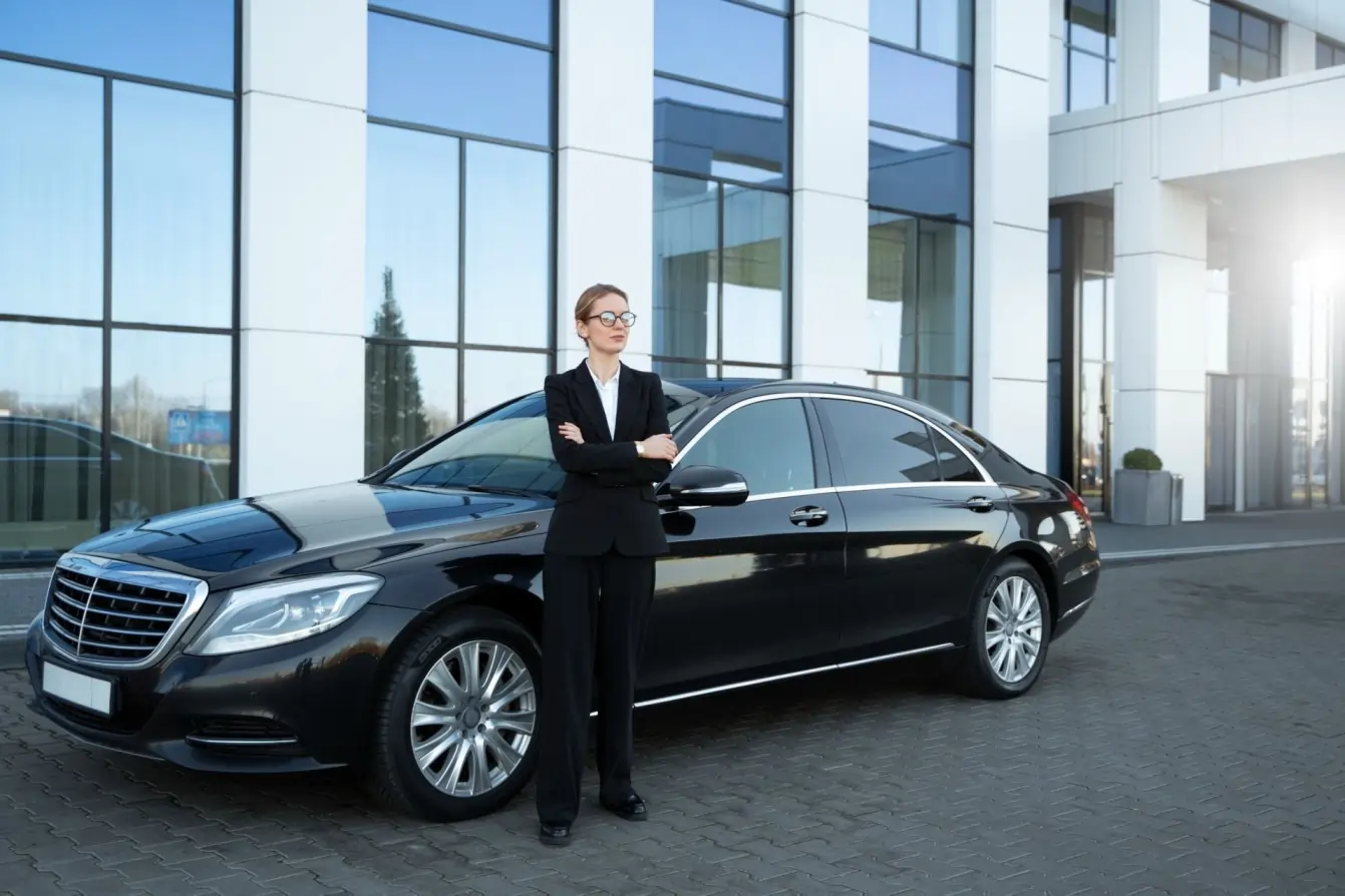 Professional female chauffeur standing with a luxury black sedan for Cambridge limo service to Toronto airport.
