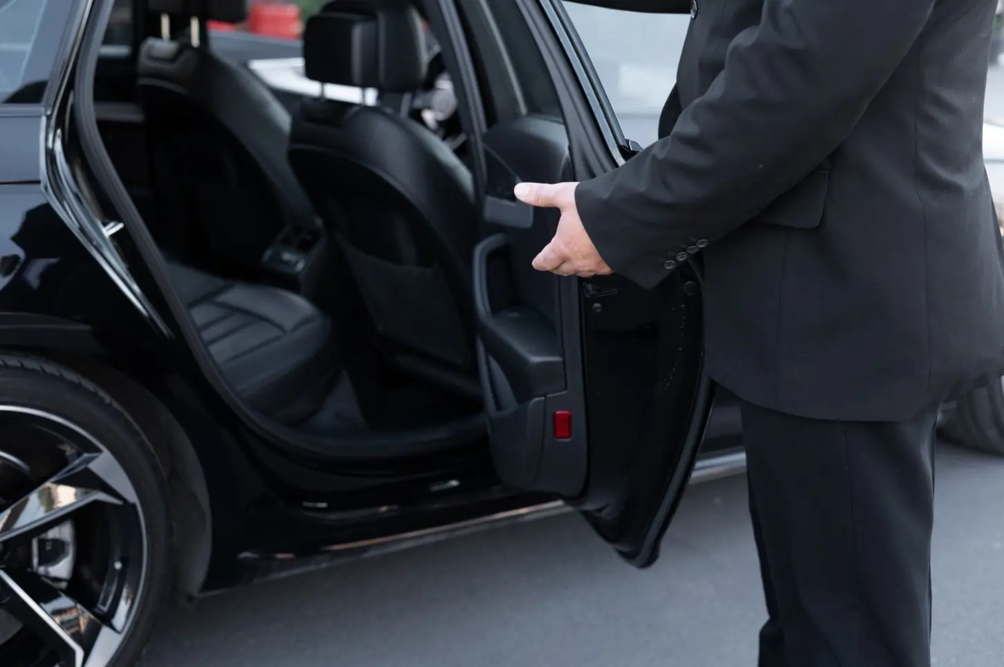 Professional chauffeur in dark suit opening passenger door of luxury black sedan for Burlington Limo Service