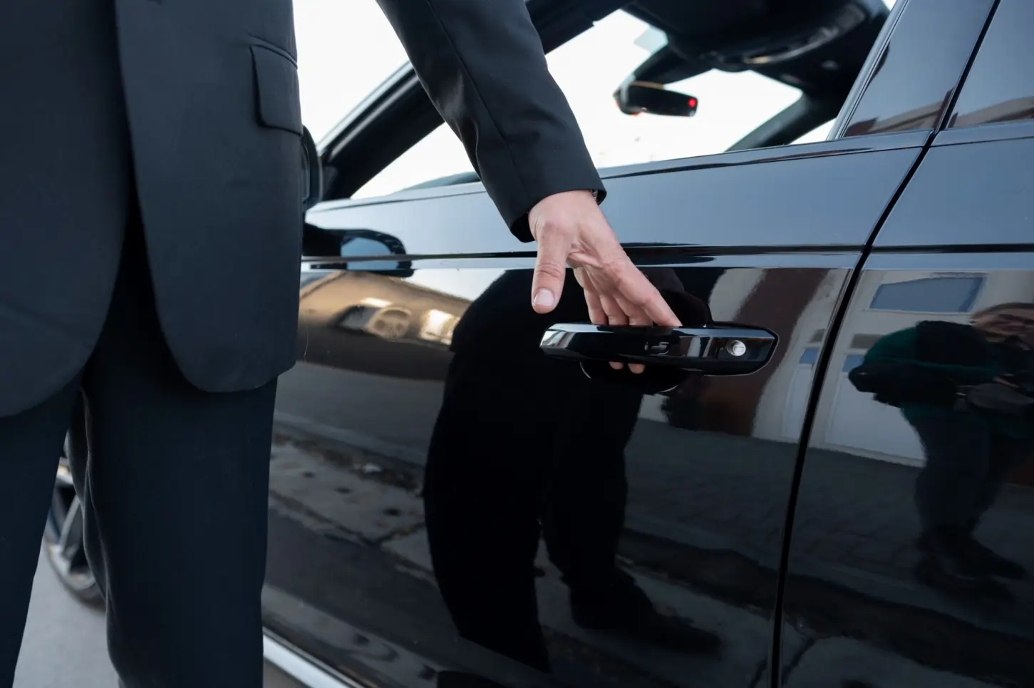 A professional chauffeur dressed in a black suit opening the door of a sleek black luxury vehicle, representing premium Bowmanville Limo Service.