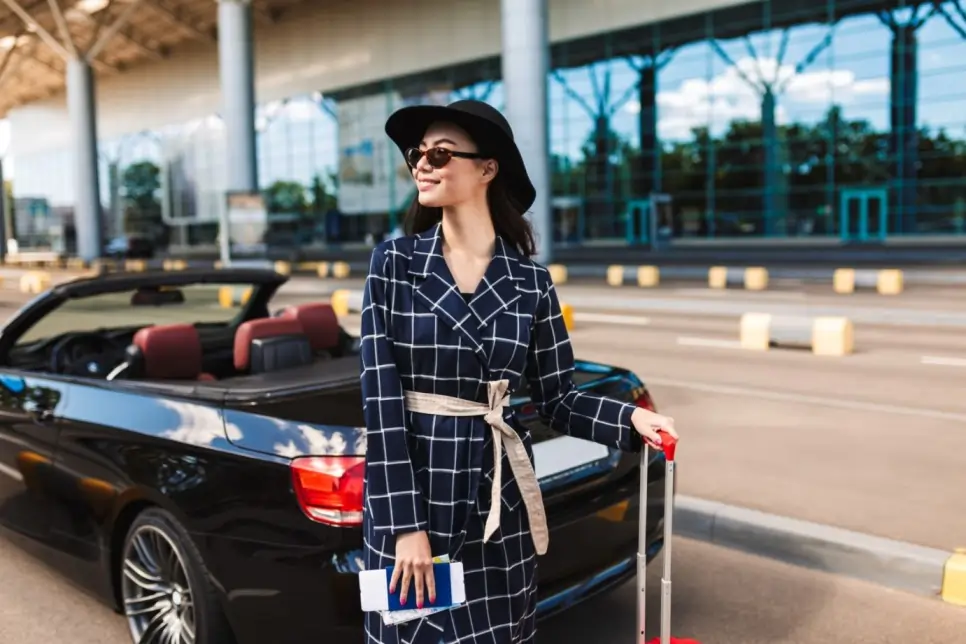 Elegant traveler with suitcase standing near a luxury car outside the airport, with reliable Markham limo service for comfortable airport transportation.